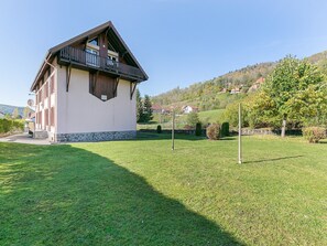 A two-story house with a balcony, surrounded by a well-maintained lawn and a hilly landscape in the background. - Spacious Apartment in La Bresse with Terrace (La Bresse)