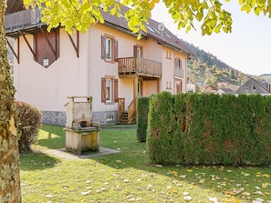 A two-story building with a balcony, a stone wall, and a well-maintained lawn. - Spacious Apartment in La Bresse with Terrace (La Bresse)