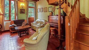 A cozy living room with a piano, leather sofas, and a wooden staircase.