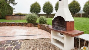 A stone patio with a built-in outdoor oven, surrounded by a stone wall and greenery.