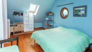 A bedroom with a bunk bed, a crib, a skylight, a shelf with clothes, a mirror, and a framed picture on the wall.
