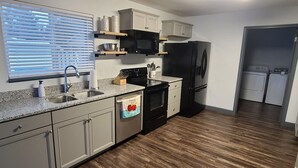 Una cocina con encimeras de granito, un lavamanos de acero inoxidable, un refrigerador negro y piso de madera.