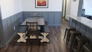 Un comedor con una mesa y sillas, un ventilador de techo, un reloj y un cuadro en la pared.