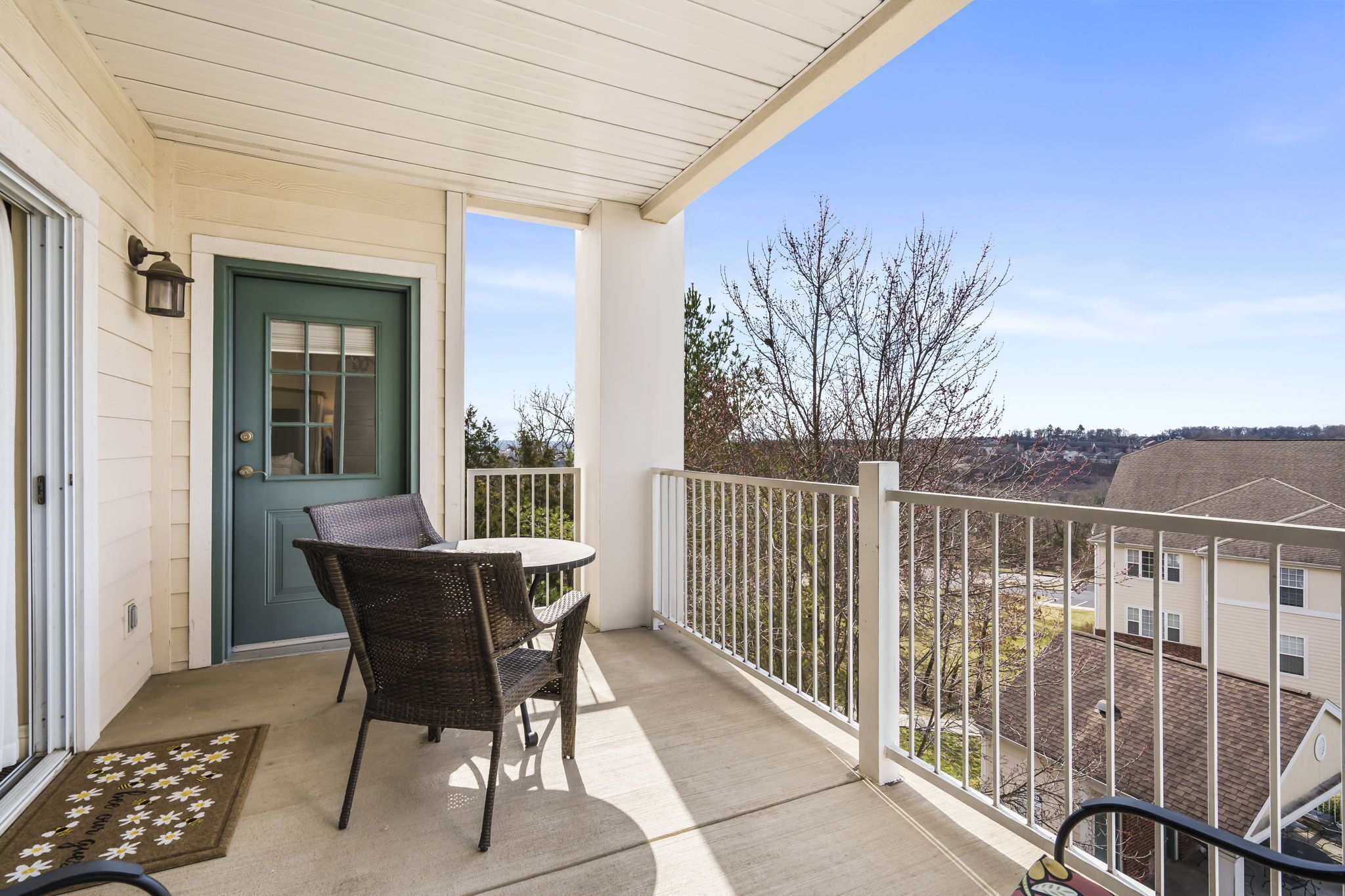 A balcony with a table and chairs, a door, and a view of the neighborhood.