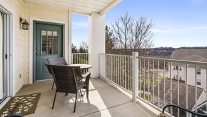 A balcony with a table and chairs, a door, and a view of the neighborhood.