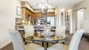 A modern kitchen with wooden cabinets, stainless steel appliances, and a glass dining table with patterned chairs.