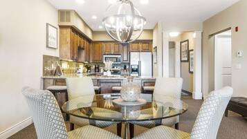 A modern kitchen with wooden cabinets, stainless steel appliances, and a glass dining table with patterned chairs.