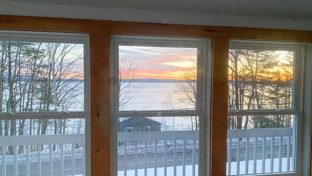 Una habitación con tres ventanas que dan a un paisaje nevado y un atardecer.