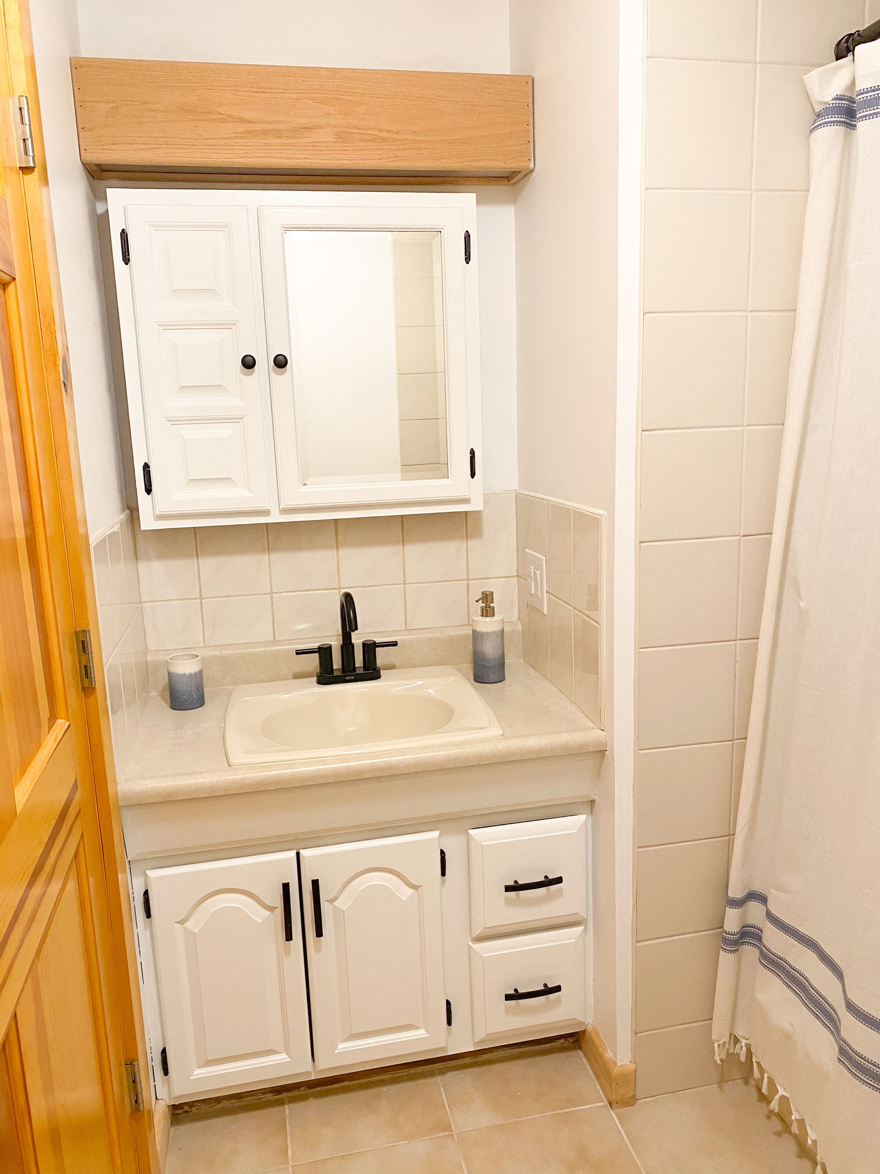 A bathroom with a white sink, mirror, and cabinets.
