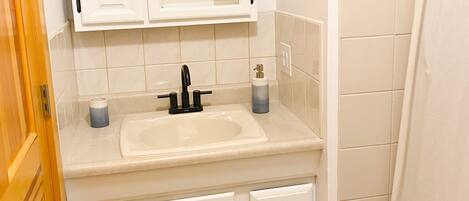 A bathroom with a white sink, mirror, and cabinets.