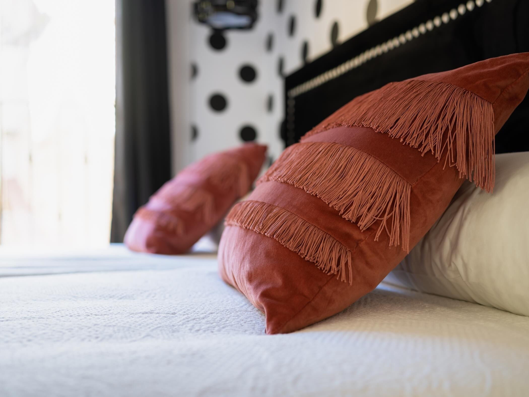 Een bed met twee kussens, waarvan er een franjes heeft.