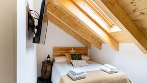Een slaapkamer met een schuine kap, een bed met een beige deken, een nachtkastje met een lantaarn, en een houten hoofdbord.