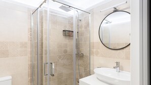 Een moderne badkamer met een douchecabine van glas, een witte wastafel en betegelde vloeren.