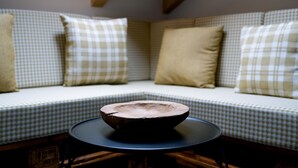 Een zithoek met een hoekbank, een geruit tafelkleed, een ronde tafel en een houten schaal als decoratie.