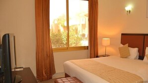 A hotel room with a bed, a desk with a television, a window with curtains, and a bedside lamp. - One to One Ain Al Fayda Resort (Al Ain)
