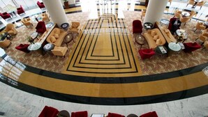 A hotel lobby with a central geometric carpet design, multiple seating areas with red and beige chairs, and a marble floor. - One to One Ain Al Fayda Resort (Al Ain)