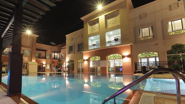 A swimming pool area with a clear water surface, surrounded by a building with multiple balconies and windows. - One to One Ain Al Fayda Resort (Al Ain)
