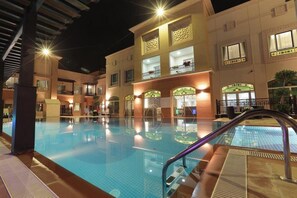 Un espace piscine avec une eau claire, entouré d’un bâtiment doté de nombreux balcons et fenêtres.