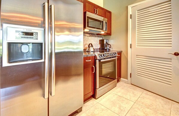 A kitchen with a stainless steel refrigerator, a microwave, a stove, and a Bosch coffee maker.