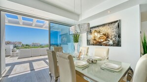 A dining area with a glass table, chairs, and a view of the cityscape through large windows. - 2288 Luxury Penthouse with Private Rooftop Pool (Estepona)