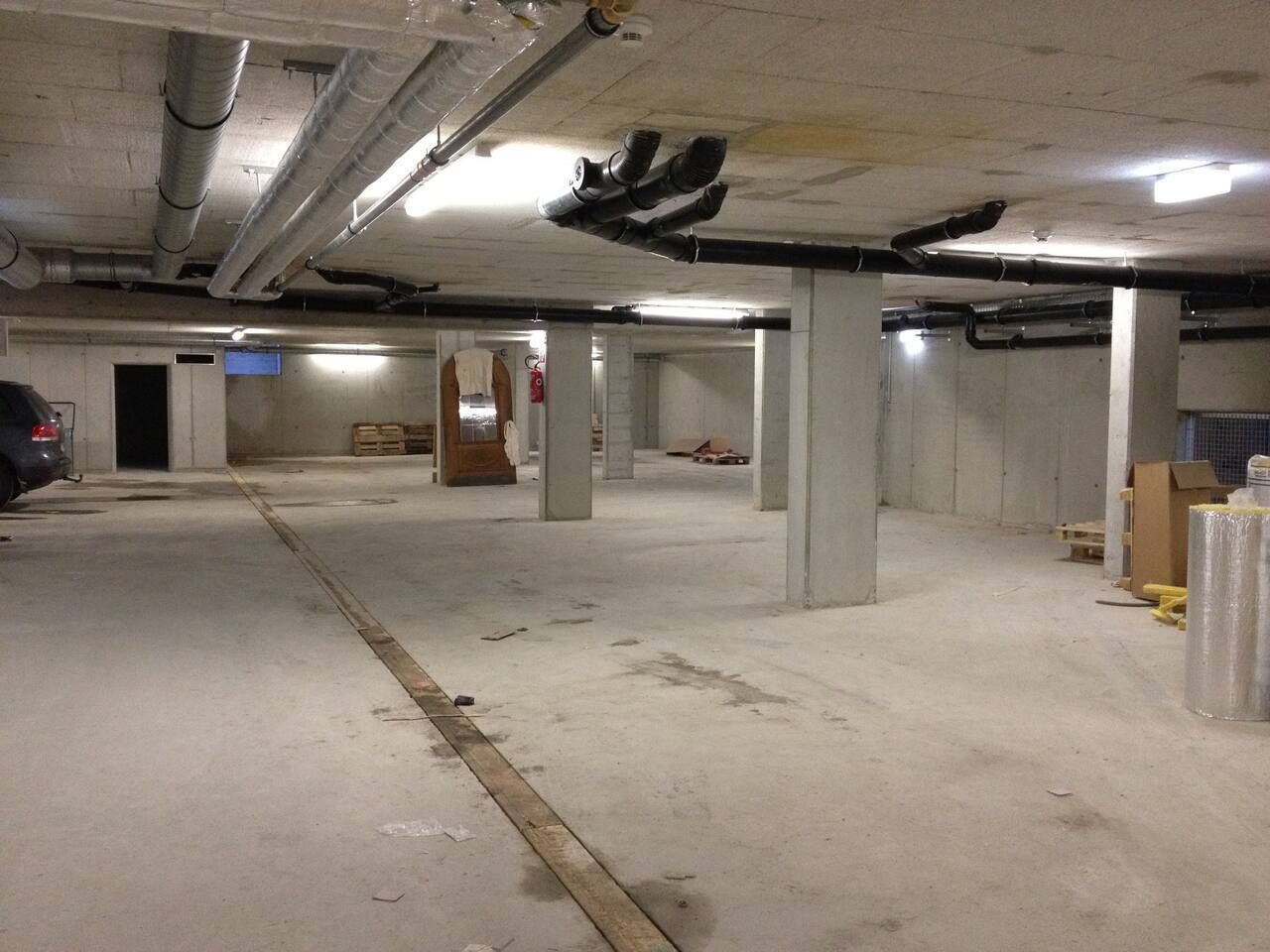 A parking garage with concrete pillars, a car, and construction materials.