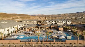 Un complexe hôtelier comprenant plusieurs bâtiments, une grande piscine centrale et un paysage montagneux en arrière-plan.