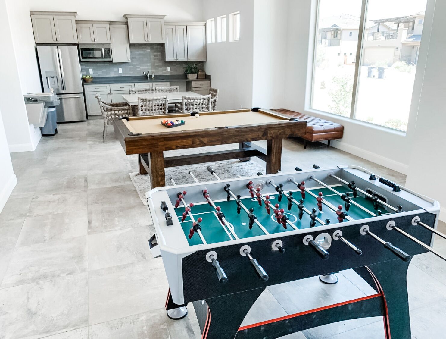 A spacious living area with a foosball table, a pool table, and a kitchen in the background.