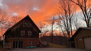 A rustic wooden building with a garage and a covered area, surrounded by trees and a sunset sky. - Private Mountain Getaway at Dogwood Hill (Rosman)
