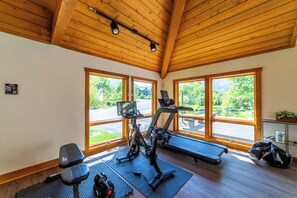 Ein Fitnessraum mit Trainingsgeräten, großen Fenstern und einer Holzbalkendecke.