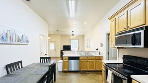 A modern kitchen with wooden cabinets, a stainless steel dishwasher, a black stove, and a dining area with a dark wooden table and chairs.