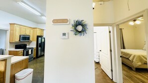 A modern kitchen with wooden cabinets, a microwave, stove, and refrigerator. There is a thermostat on the wall and a decorative wreath.