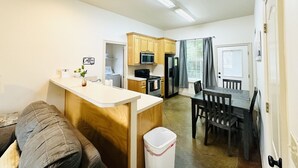 A compact kitchen with wooden cabinets, a microwave, a refrigerator, and a dining area with a table and chairs.