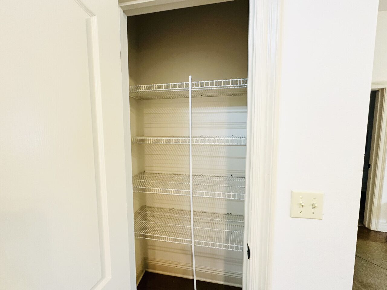 A walk-in closet with metal shelving units and a light switch on the wall.