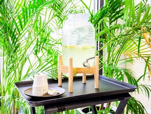 Un frasco de vidrio grande lleno de un líquido amarillento sobre un soporte de madera, colocado sobre una mesa negra con una bandeja que contiene tazas blancas y una cáscara de plátano.