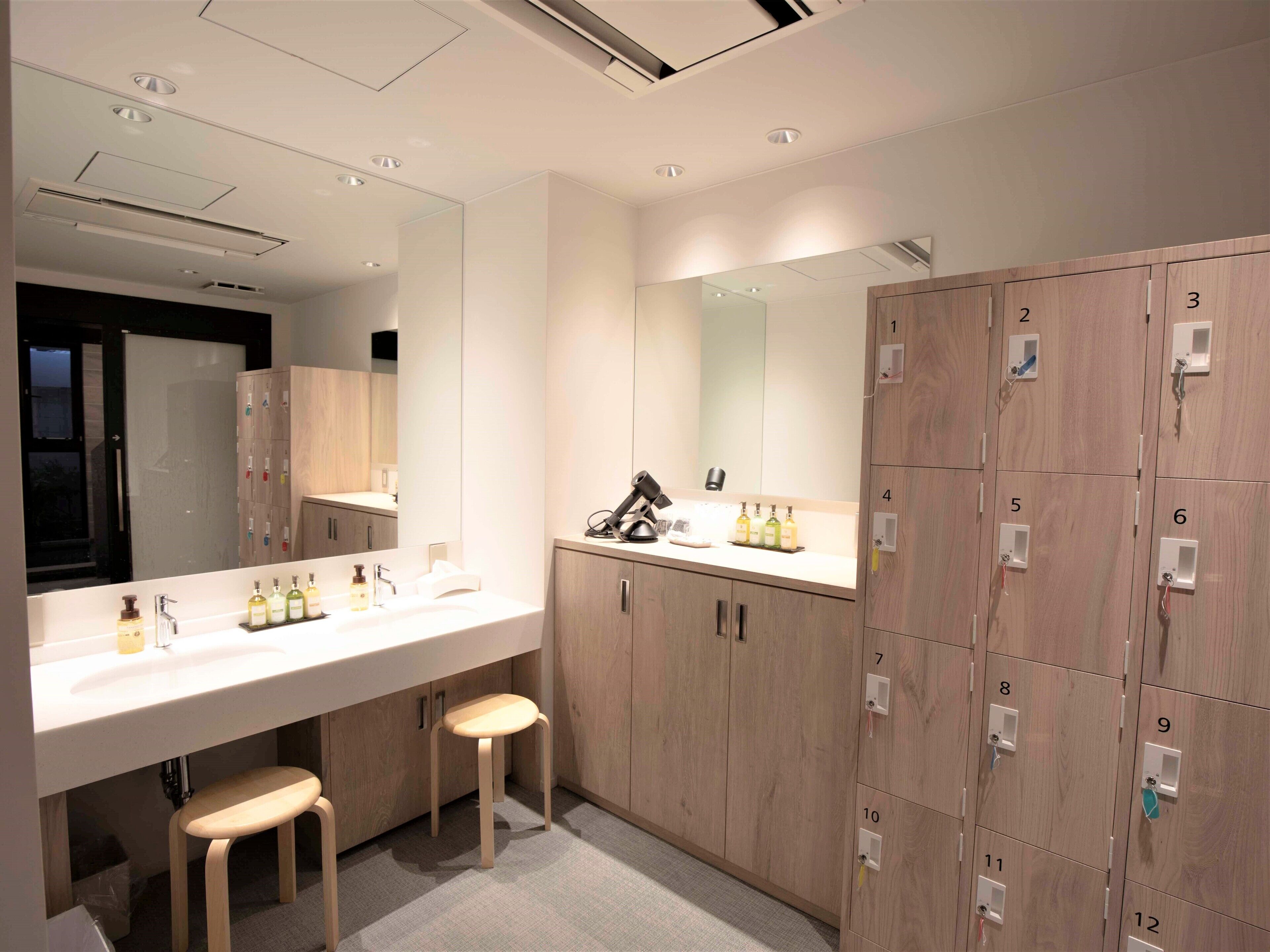 A modern bathroom with a large mirror, a vanity with a sink, and a row of lockers.