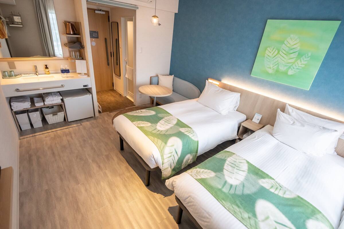 A hotel room with two beds, a desk, a chair, and a small table.