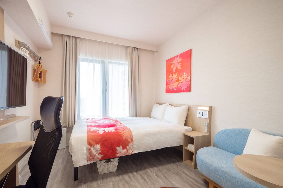 A hotel room with a bed, a desk, a chair, a sofa, and a small table.