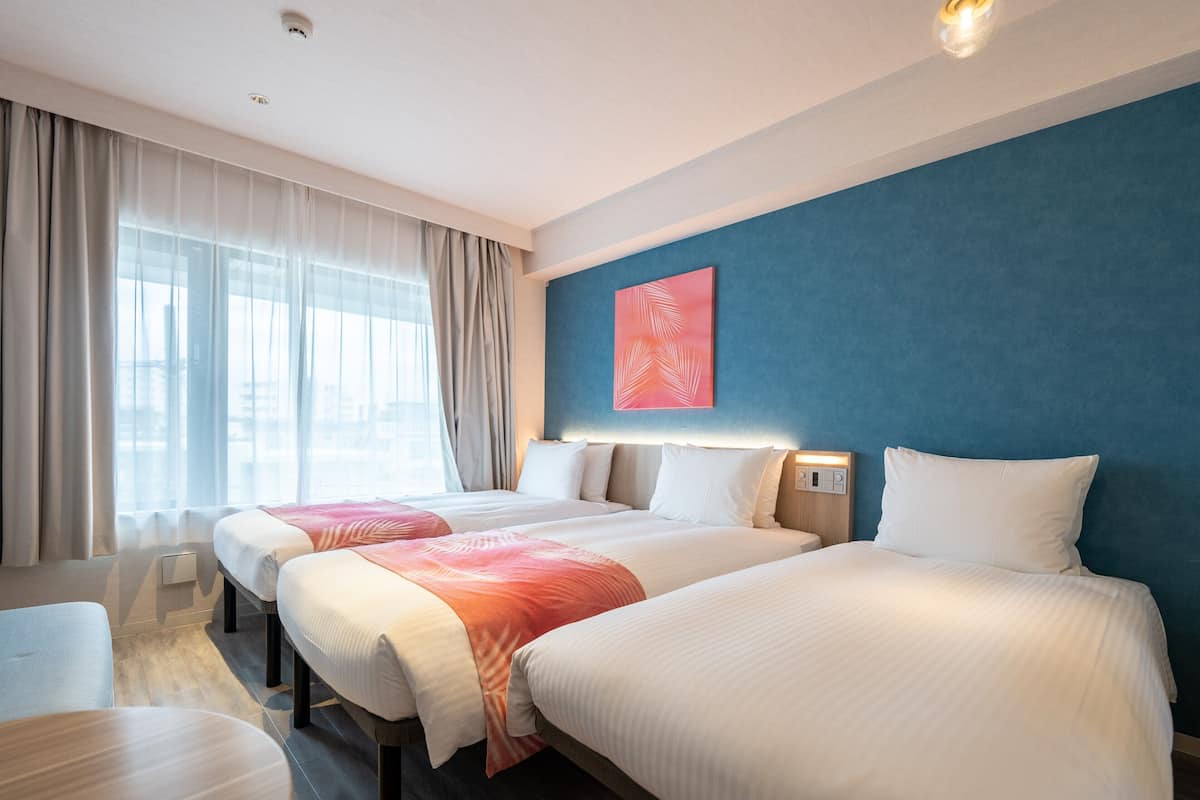 A hotel room with two beds, a desk, and a large window with curtains.