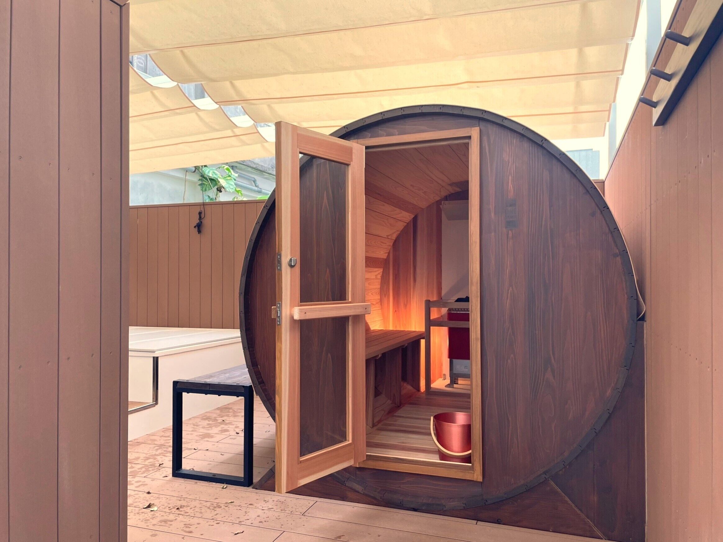 Ein raundes Zimmer aus Holz mit einer geöffneten Tür, durch die ein Bett und ein roter Eimer zu sehen sind.
