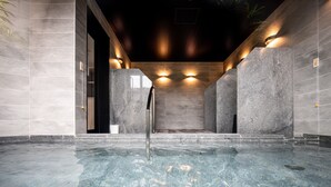 An indoor swimming pool with a clear water surface, surrounded by stone walls and equipped with wall-mounted lights. - Tabino Hotel lit Miyakojima (Miyakojima)