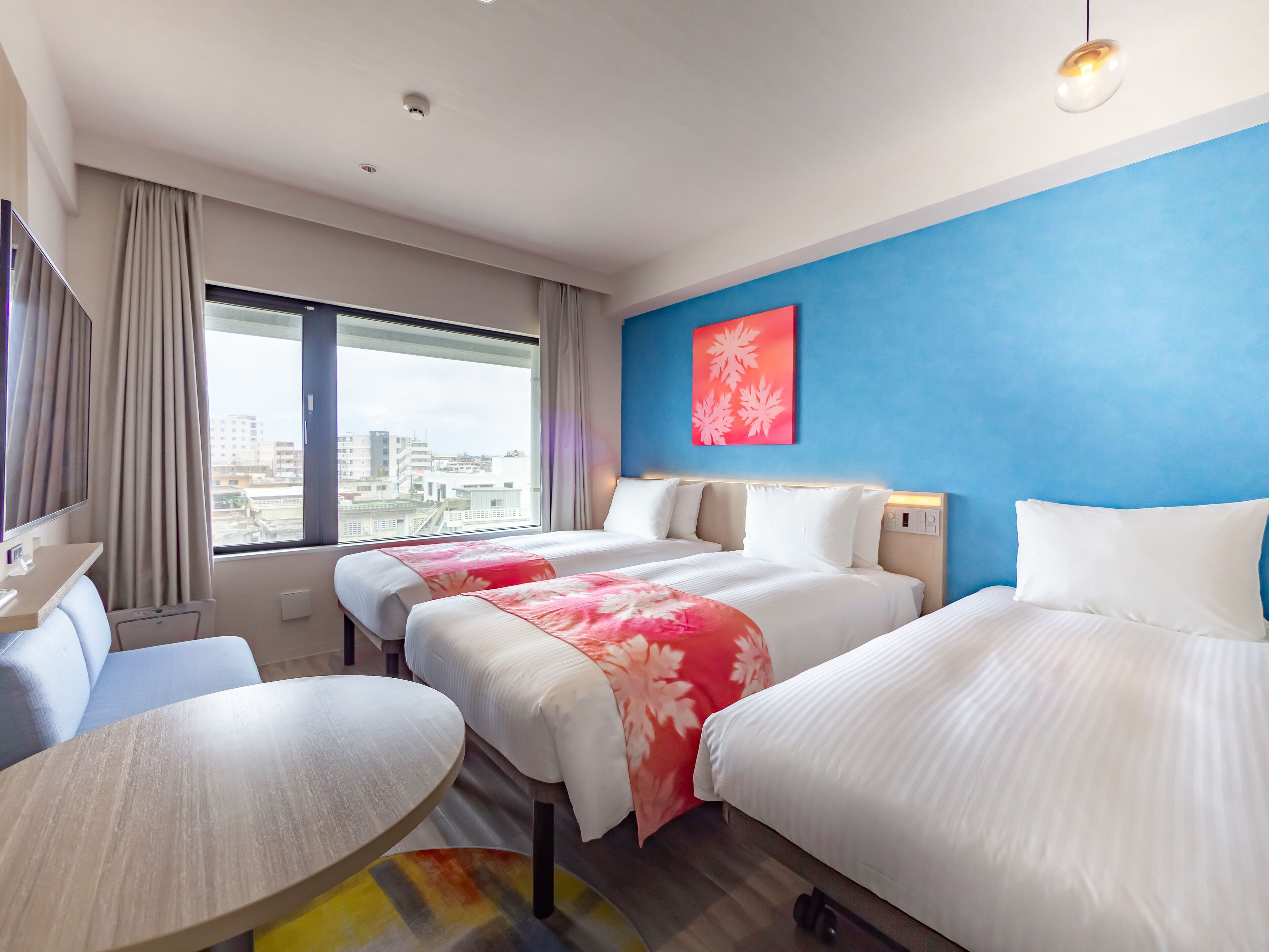 A hotel room with two beds, a desk, and a view of the city.