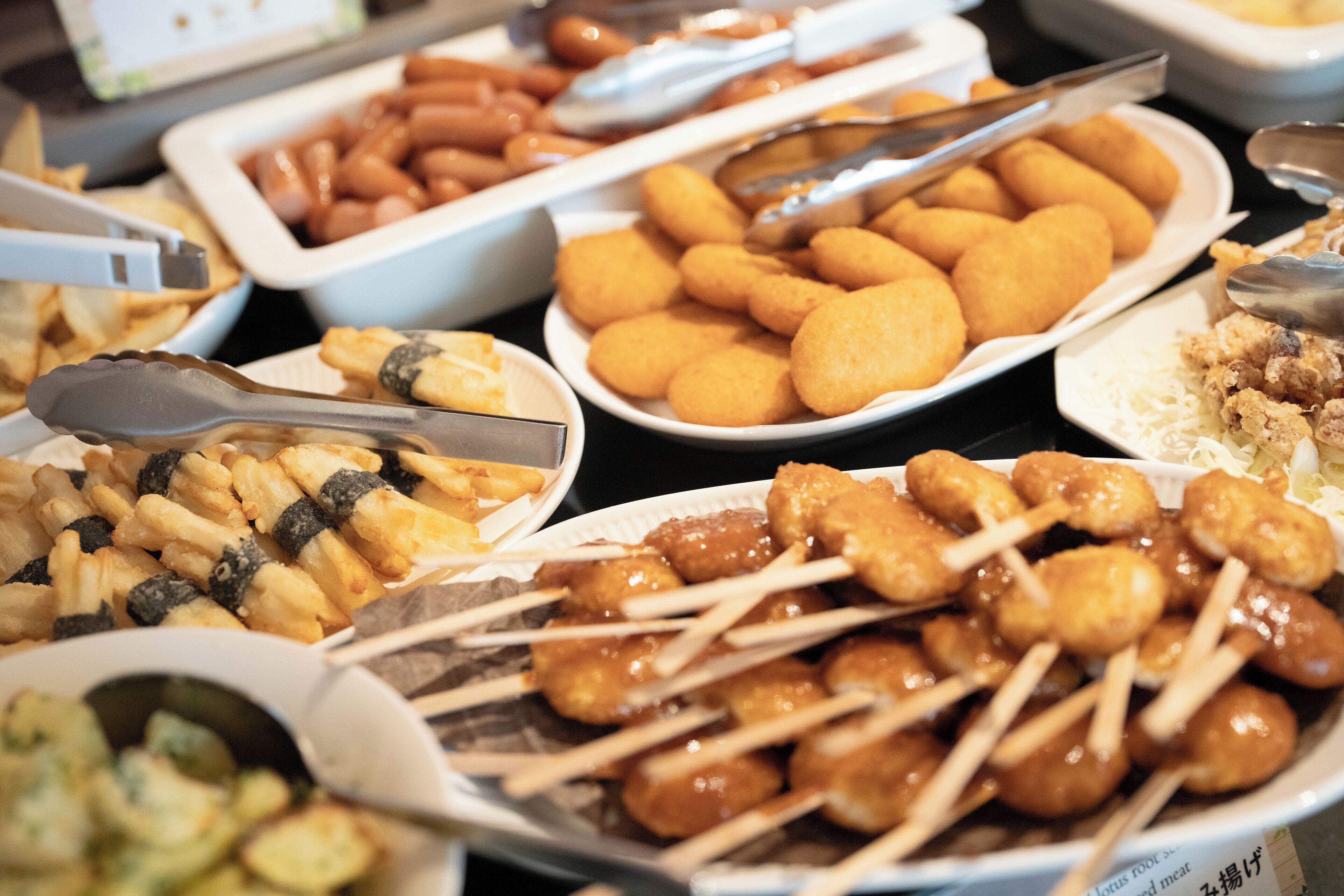 A buffet with various food items including fried snacks, skewers, and a dish with shredded meat.