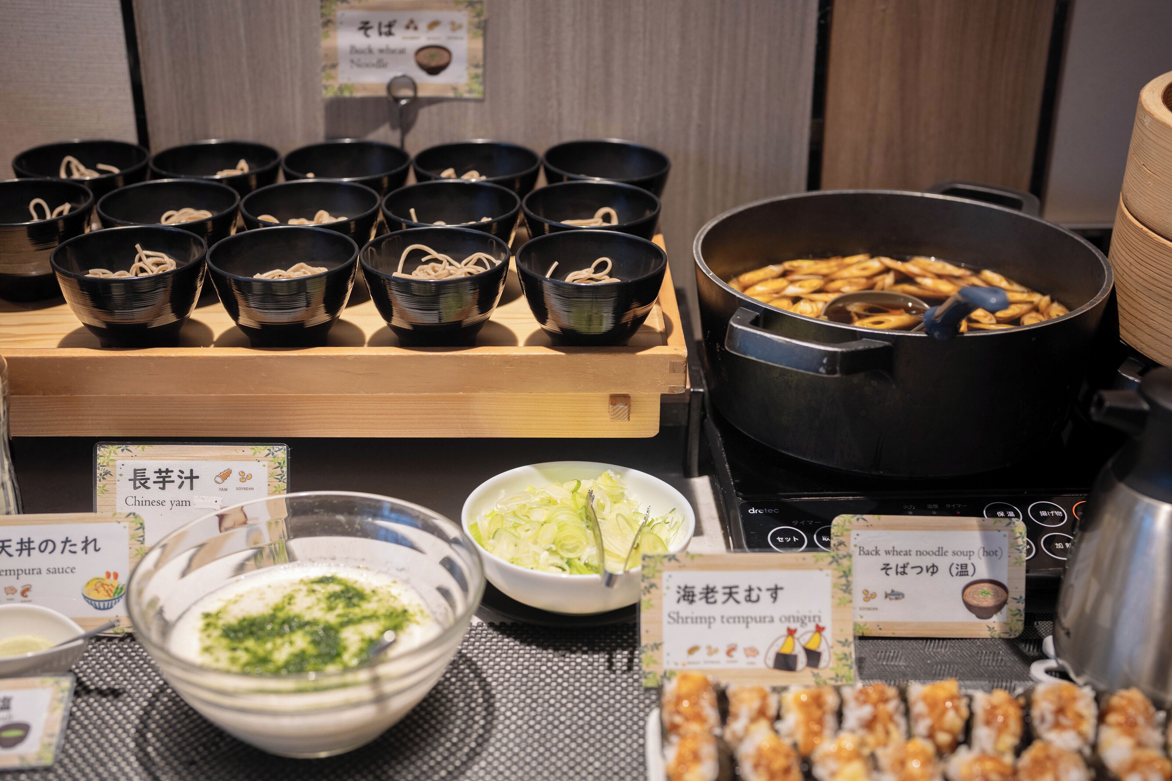 A variety of Asian dishes, including noodles and tempura, served in black bowls and a large pot.