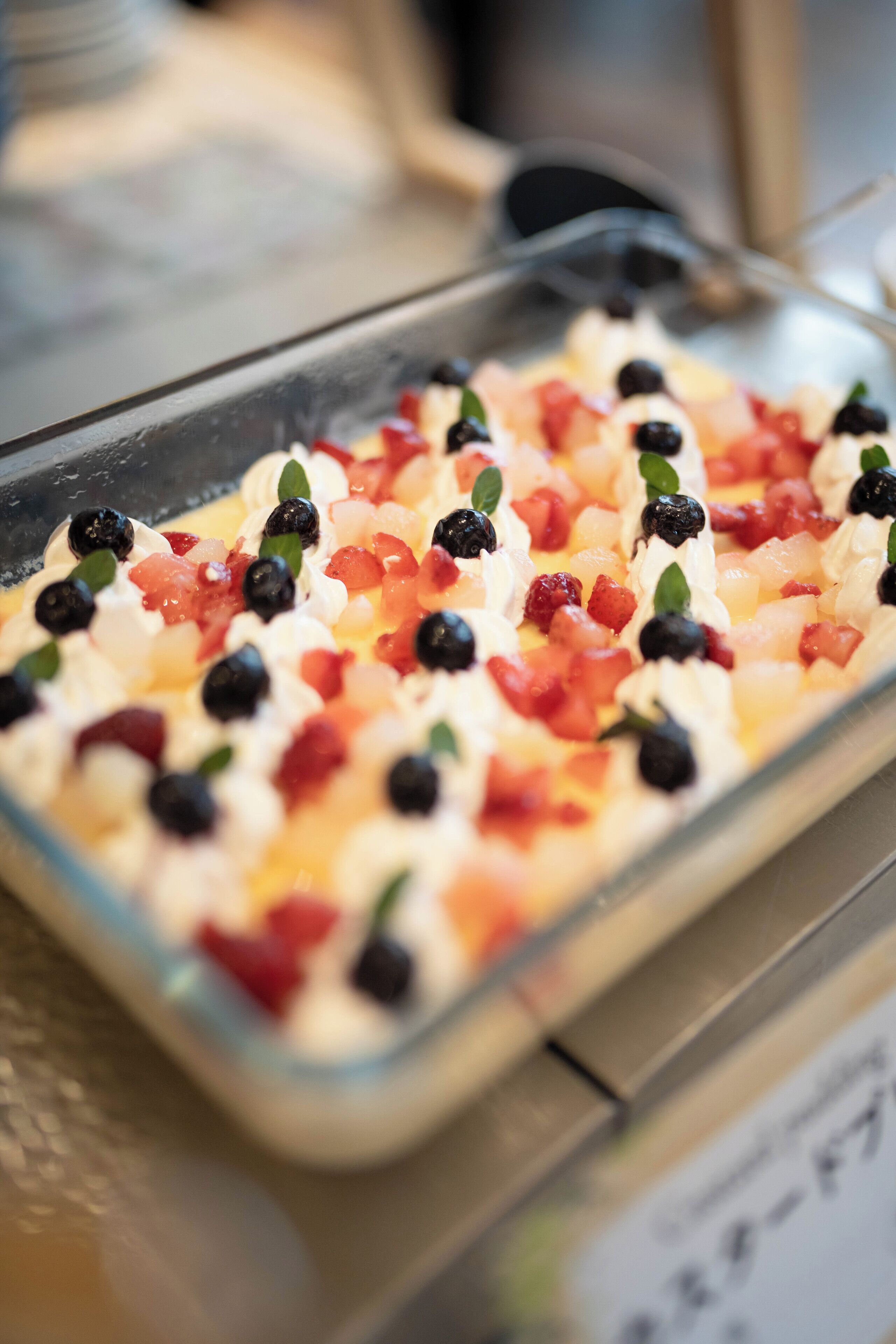 Postre en un recipiente de vidrio con crema batida, arándanos y fruta picada.