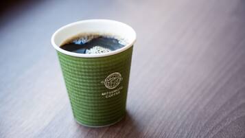 A green paper cup with a logo and text, containing a dark liquid, likely coffee, on a wooden surface.