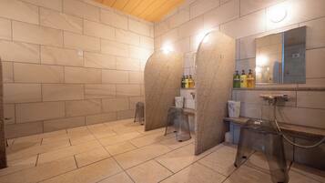A modern bathroom with beige tiles, a wooden ceiling, and a mirror with toiletries on the counter.