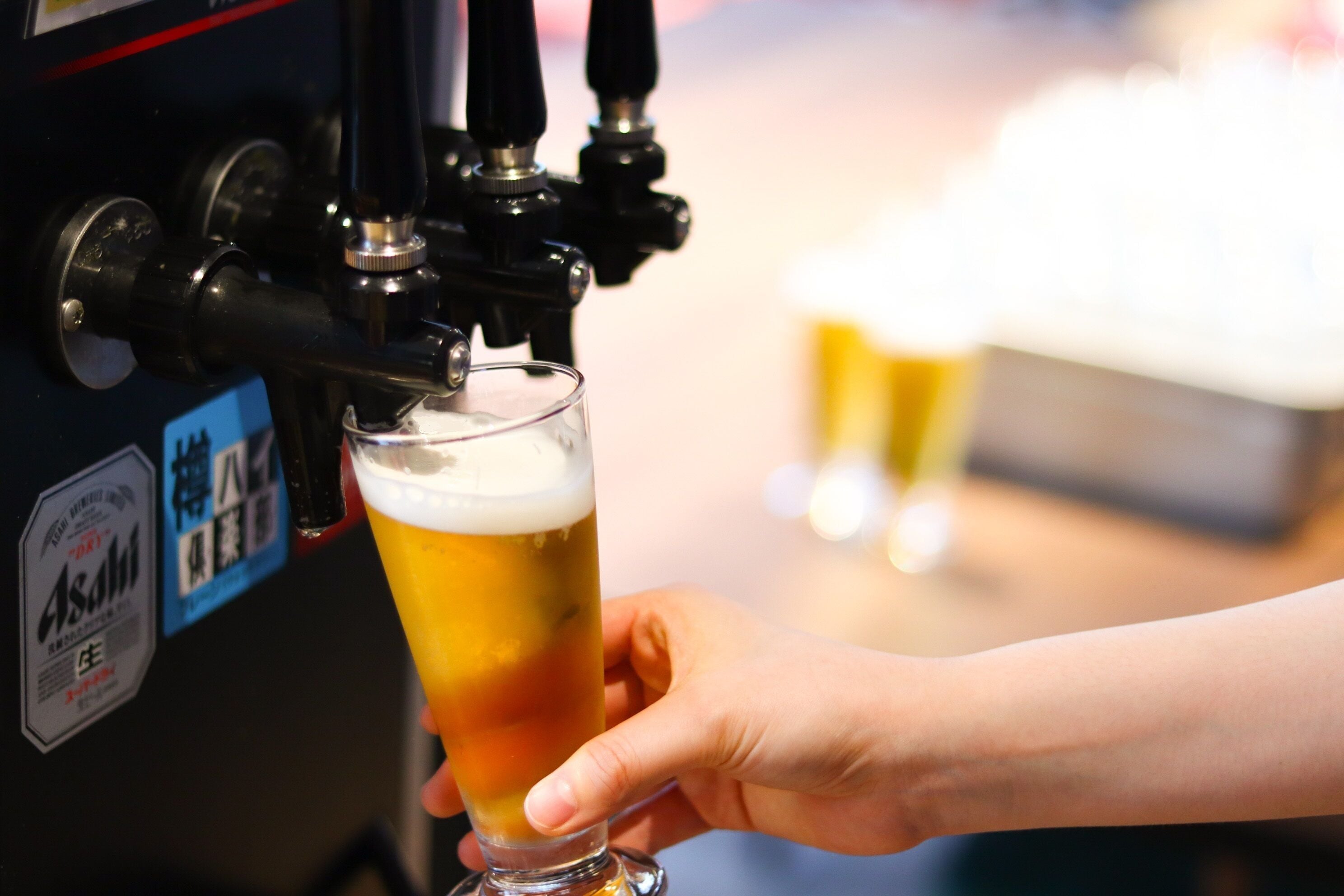 A hand holding a glass of beer at a tap.