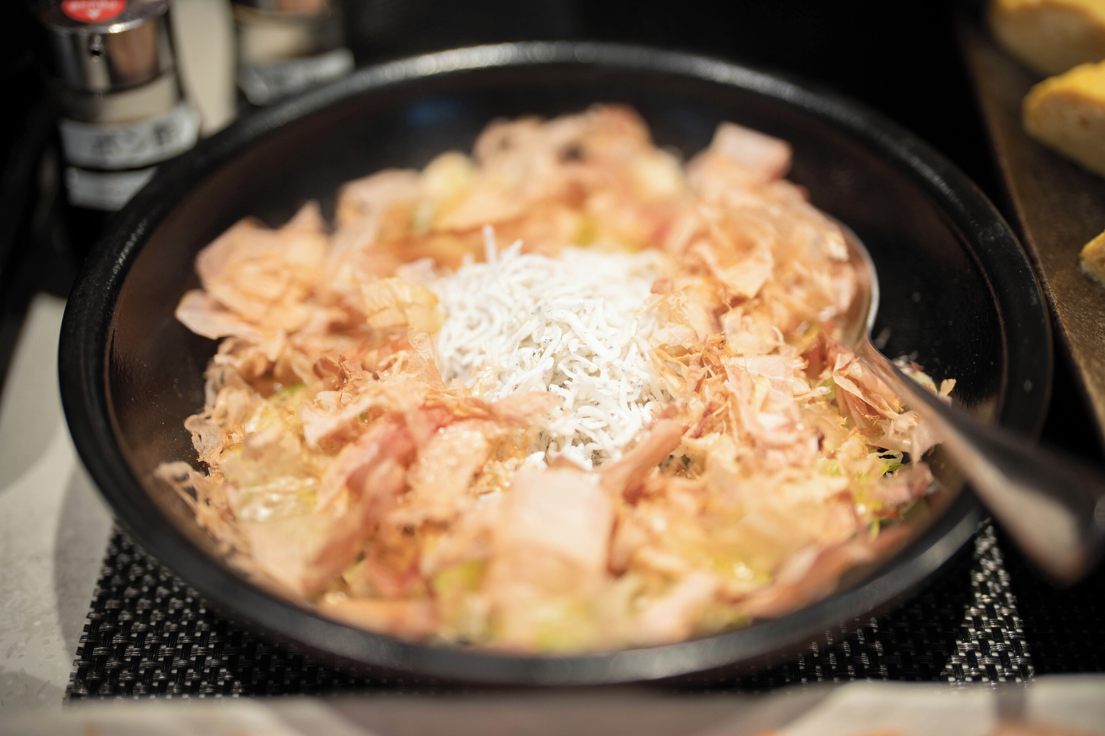 A pan with a mixture of ingredients, including shredded cheese and possibly meat, on a stove.