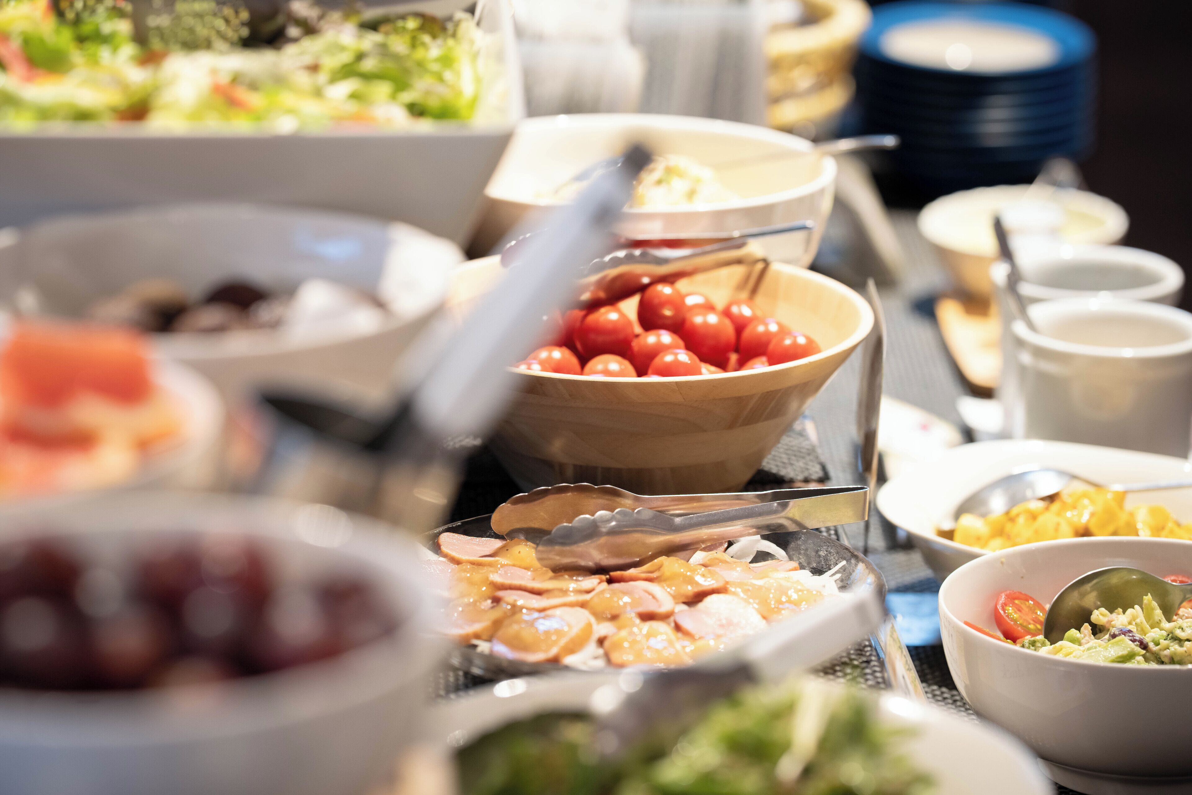 Un buffet proposant divers plats, notamment un saladier de tomates cerises, un plateau de charcuteries et un saladier de salade.