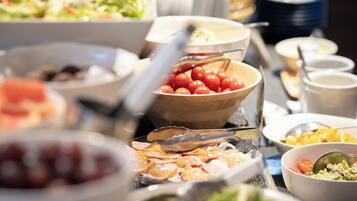 Un buffet proposant divers plats, notamment un saladier de tomates cerises, un plateau de charcuteries et un saladier de salade.